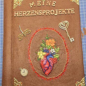 Warum habe ich das Buch so gestaltet?
Braun: ist die Erde . Ich stehe mit beiden Beinen darauf.
Das Herz: Ursprung des Lebens, es entscheidet über Leben,Tod und Gefühl.
Die Blumen und die Libelle :
stehen für Natur und Wiedergeburt
Der Schlüssel :
steht für die vielen Geheimnisse im Leben,die erforscht werden wollen.
Glitzersteine:
Ist das kleine Feuerwerk was manche Sachen auslösen. Wie ein Kuss meines geliebten Mannes ,eine Überraschung oder eine unerwartete Freude.
Das Garn:
Ist der Faden des Lebens ,der stetig weiter läuft bis am Ende die Spule alle ist.
Die Zeit:
schreitet vorran und bestimmt mein Leben.
Es ist ein sehr persönlich gestaltetes Buch .
Ich möchte darin meine kleinen Stickereien aufbewahren, damit sie nicht unsere Wände zu pflastern und irgendwann nicht mehr gesehen werden.