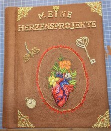 Warum habe ich das Buch so gestaltet?
Braun: ist die Erde . Ich stehe mit beiden Beinen darauf.
Das Herz: Ursprung des Lebens, es entscheidet über Leben,Tod und Gefühl.
Die Blumen und die Libelle :
stehen für Natur und Wiedergeburt
Der Schlüssel :
steht für die vielen Geheimnisse im Leben,die erforscht werden wollen.
Glitzersteine:
Ist das kleine Feuerwerk was manche Sachen auslösen. Wie ein Kuss meines geliebten Mannes ,eine Überraschung oder eine unerwartete Freude.
Das Garn:
Ist der Faden des Lebens ,der stetig weiter läuft bis am Ende die Spule alle ist.
Die Zeit:
schreitet vorran und bestimmt mein Leben.
Es ist ein sehr persönlich gestaltetes Buch .
Ich möchte darin meine kleinen Stickereien aufbewahren, damit sie nicht unsere Wände zu pflastern und irgendwann nicht mehr gesehen werden.